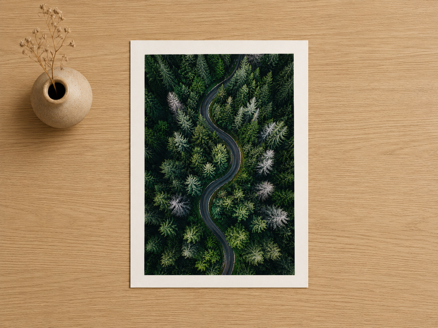 Beyaz matla sunulan, kuş bakışı orman ve yol manzarasını gösteren baskı poster.
