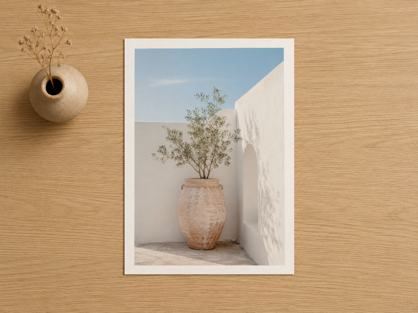 Beyaz çerçeveli poster, ahşap masada sergilenen, toprak tonlu çömlekçi saksıda saksı ve bitki detayı gösteren sanat baskısı.