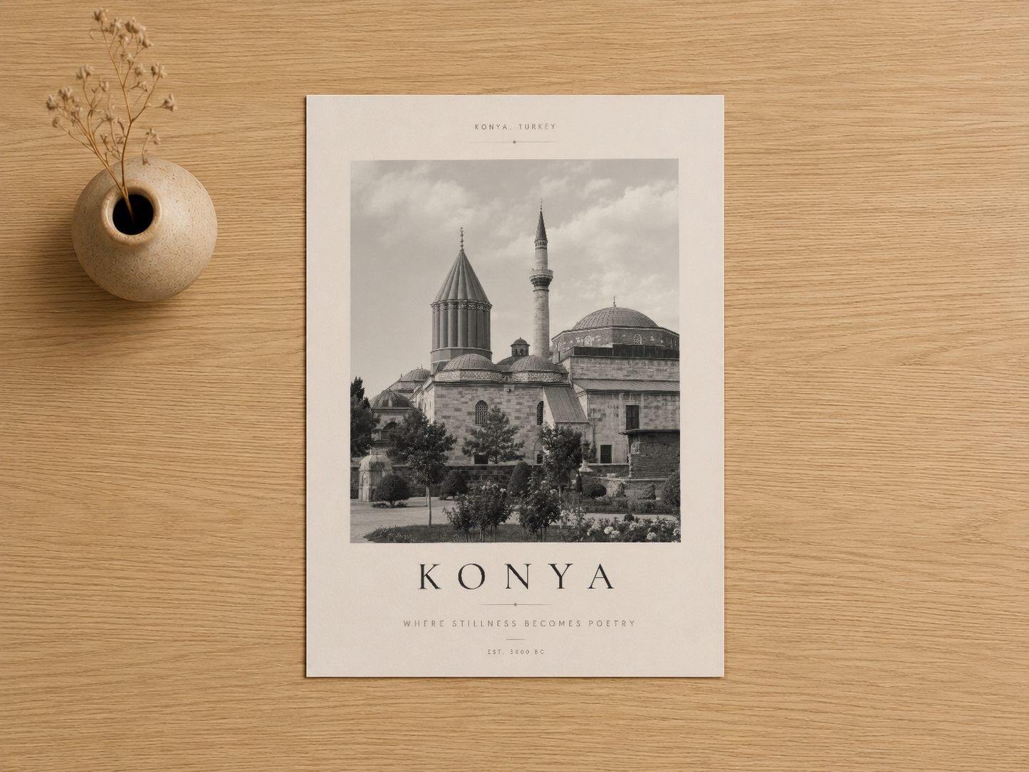 Konya Türkiye mimarı siyah beyaz poster, krem çerçevede, ahşap zemin üstünde, yanında seramik vazo.