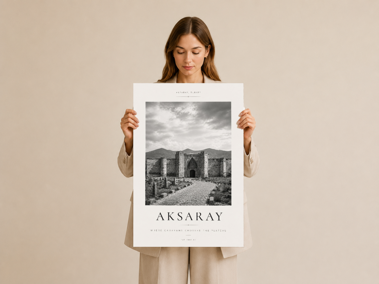 Aksaray tablosu, kadın tarafından tutulan beyaz çerçeveli poster, tarihi mimariyi zarif tipografiyle sunan sanat eseri.