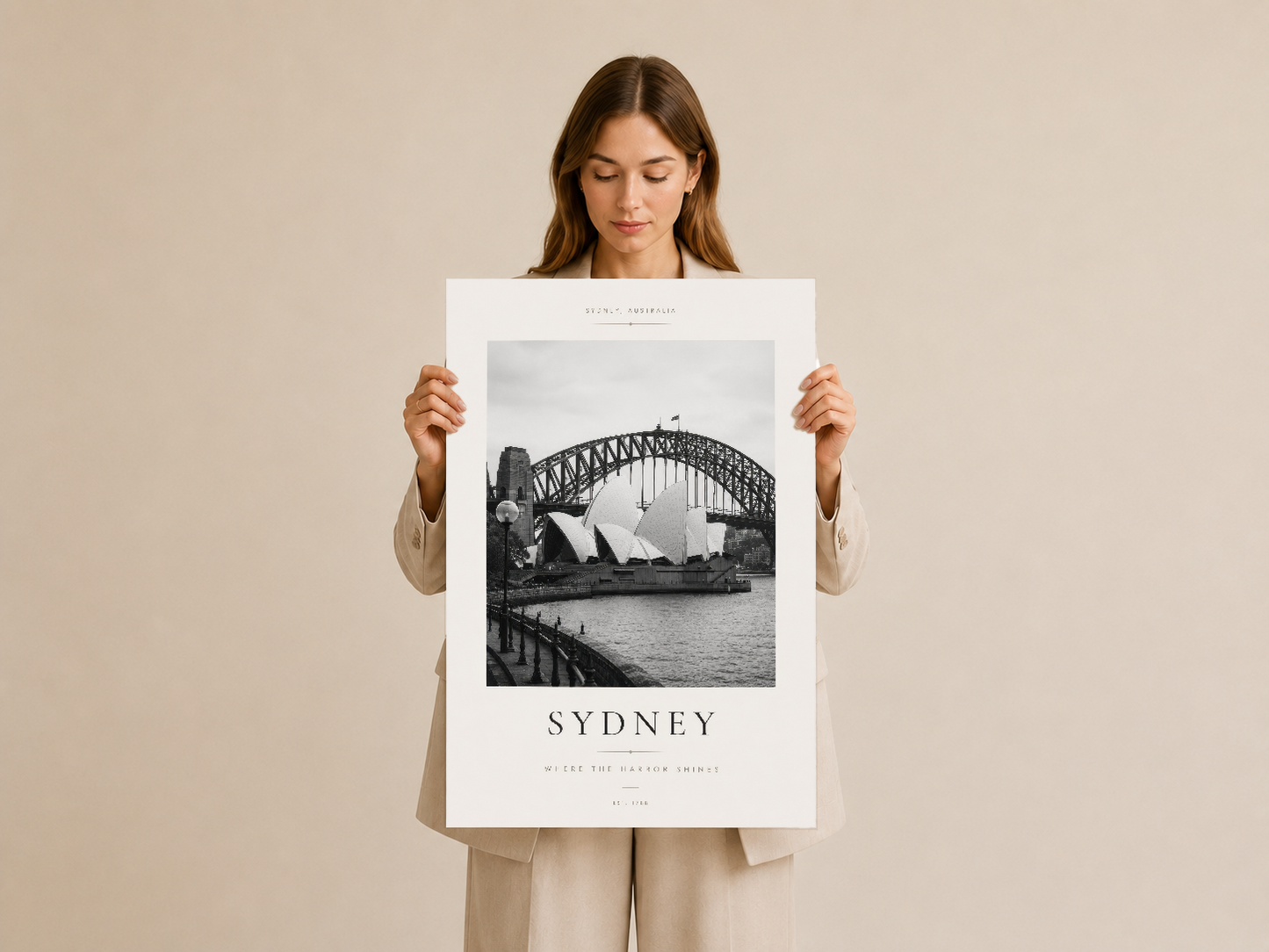 Kadının tuttuğu Sydney şehri tablosu, ikonik köprü ve bina fotoğrafıyla zarif bir yer tutucu tasarımı.