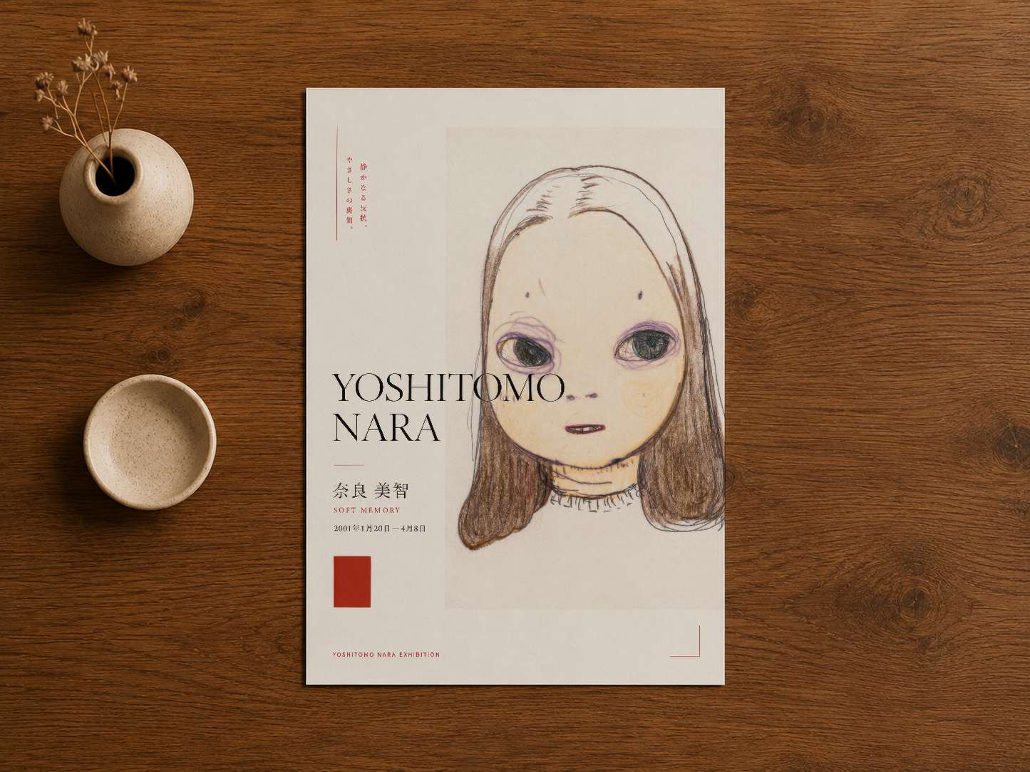 Yoshitomo Nara afişi ahşap masa üzerinde, seramik aksesuarlar yanında, minimalist sanat sunumu.