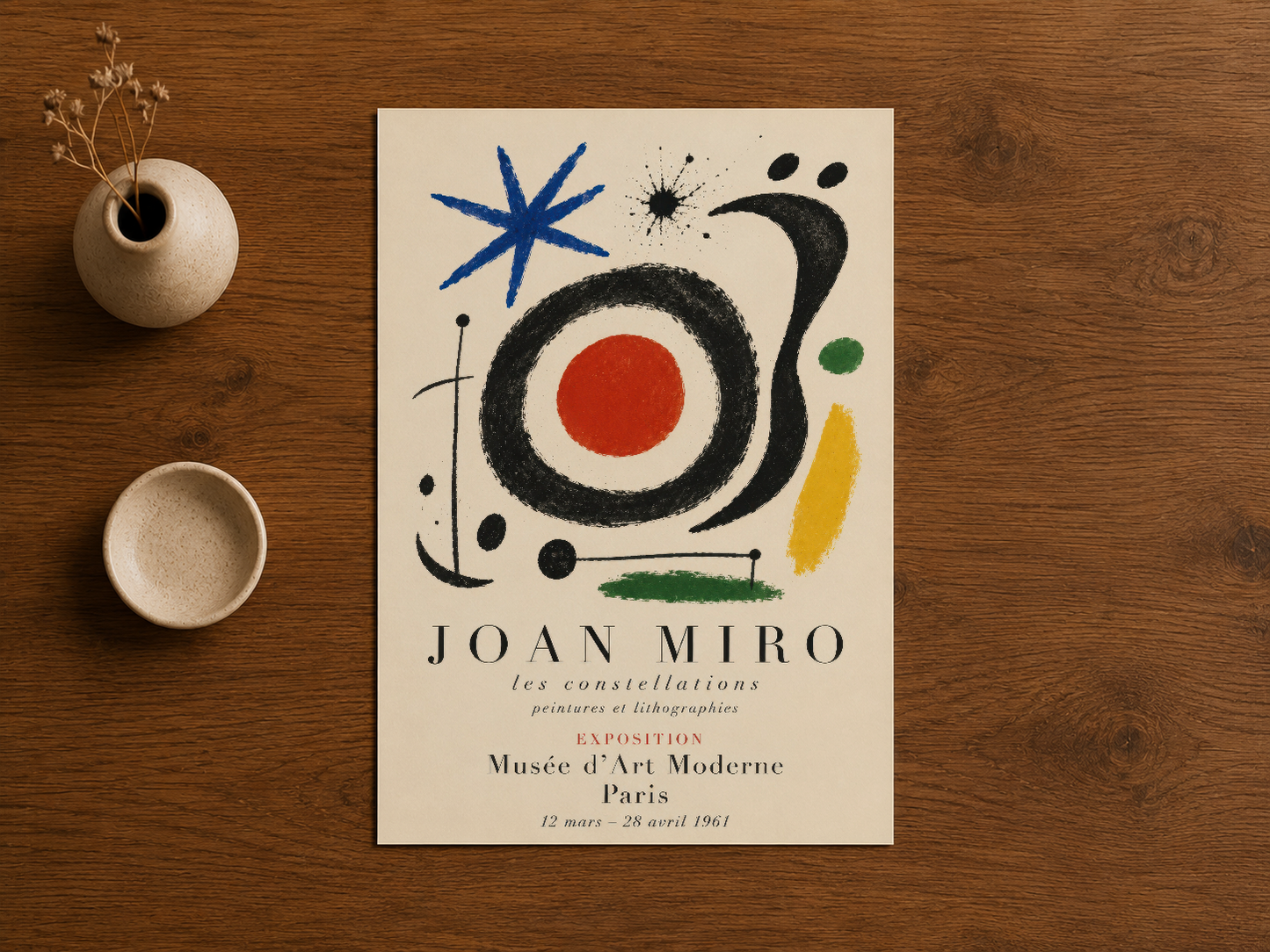 Ahşap masanın üzerinde sergilenen Joan Miró'nun sanat posteri ve minimal ev dekorasyon aksesuarları.