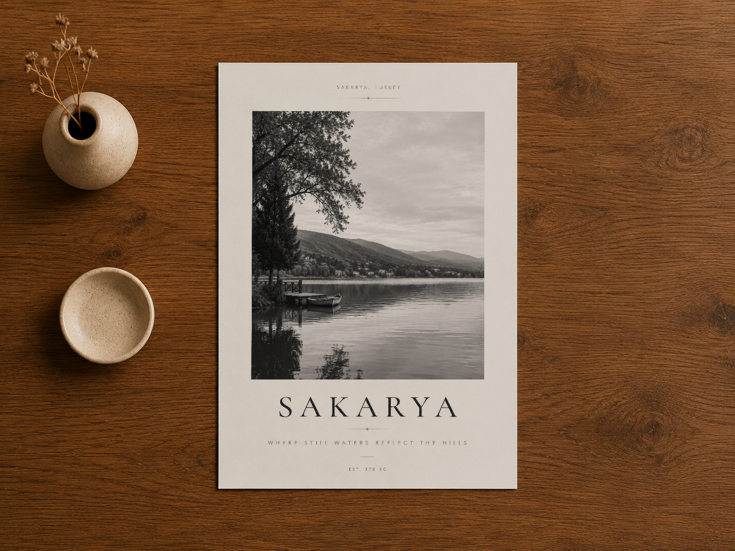 Sakarya siyah beyaz poster ahşap yüzeyde, seramik aksesuarlar ve kurutulmuş çiçeklerle.
