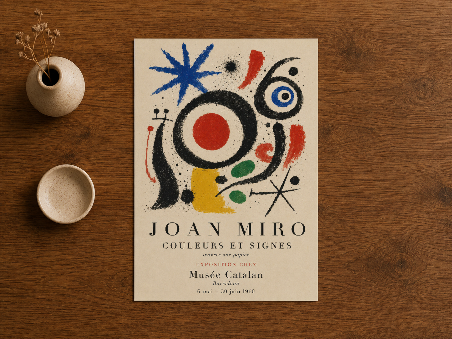 Joan Miro'nun 1960 sergi afiş tasarımı, ahşap masa üzerinde sakin minimalist dekorasyonla çerçeveleniyor.