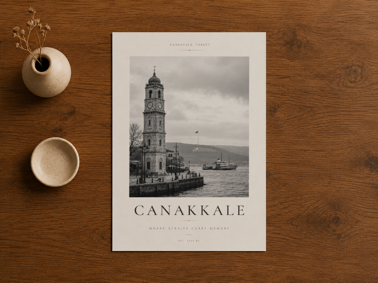 Çanakkale siyah beyaz baskısı, doğal ahşap masada minimal tasarım aksesuarları ile sunulan sanat eseri.