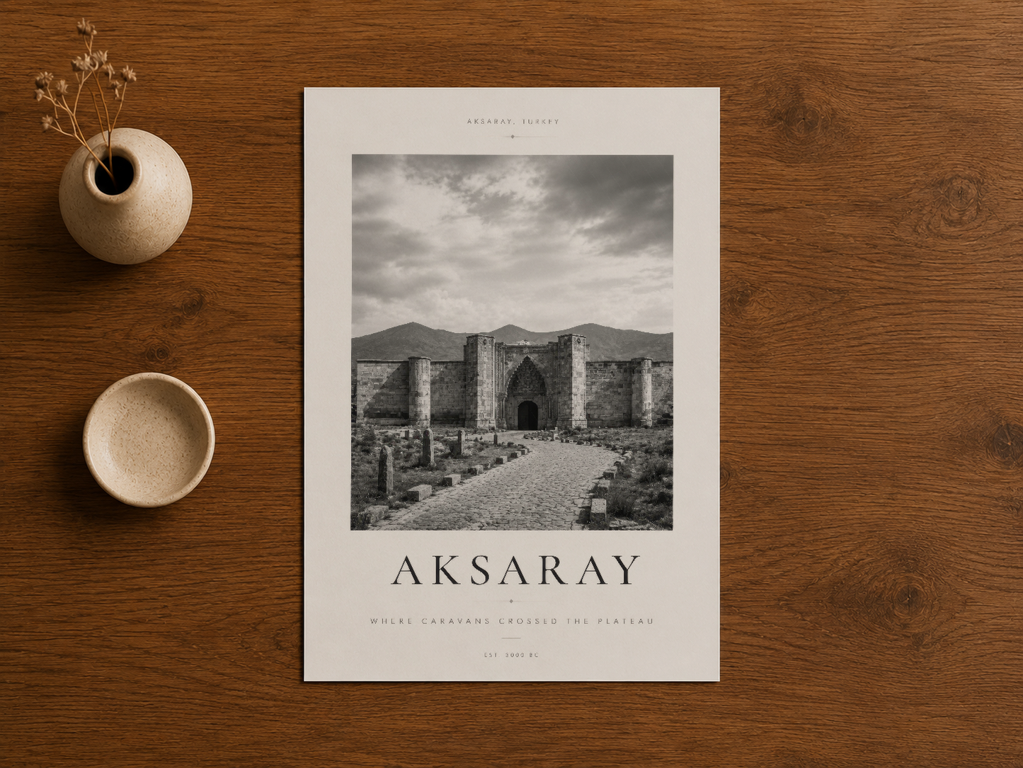 Aksaray poster, ahşap zeminde, doğal vazo ve bitki aksessuarlarıyla gösterilen siyah beyaz sanat baskısı.