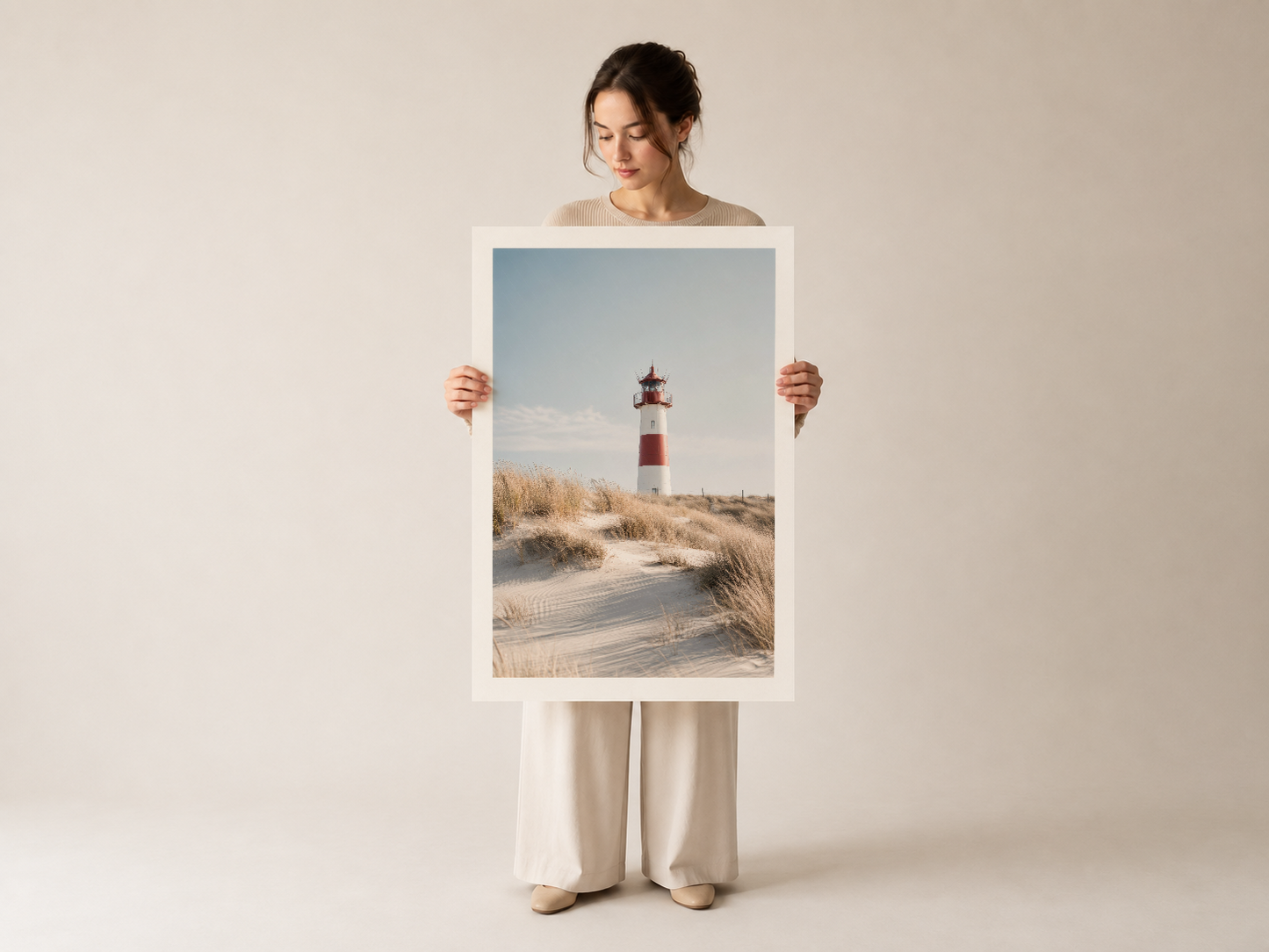 Kırmızı-beyaz feneri sahil manzarasında gösteren poster, nötr giysileriyle bir kadın tarafından gösterilmekte olan sanat