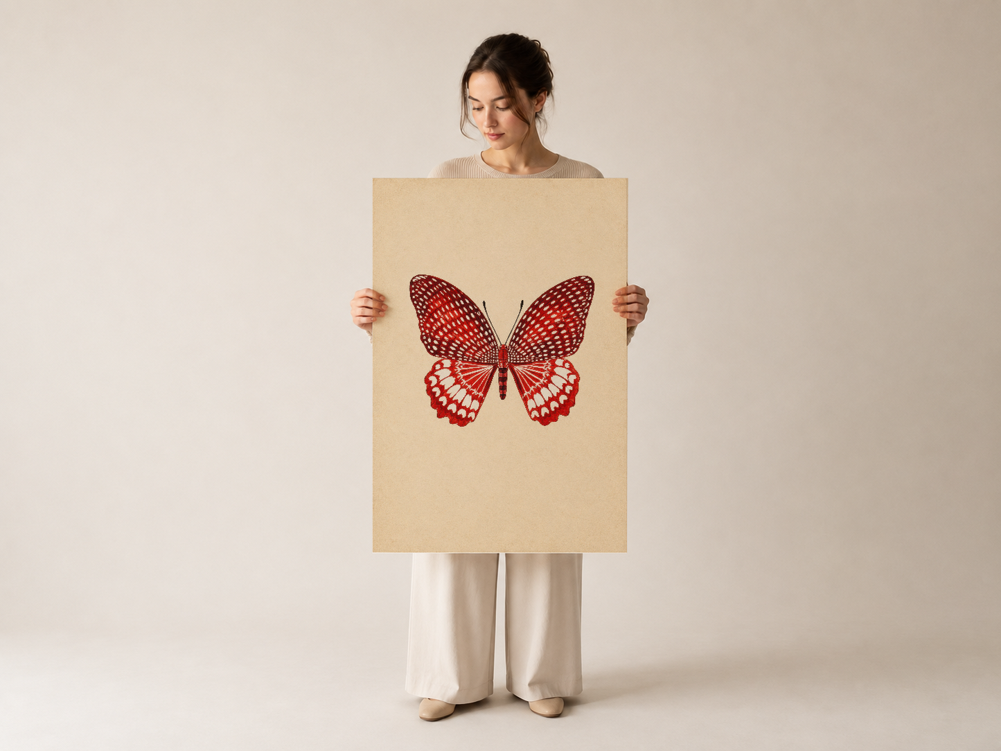Nötr arka planda duran kişinin elleriyle tuttuğu, minimalist tarzda kırmızı kelebek motifli sanat baskısı.