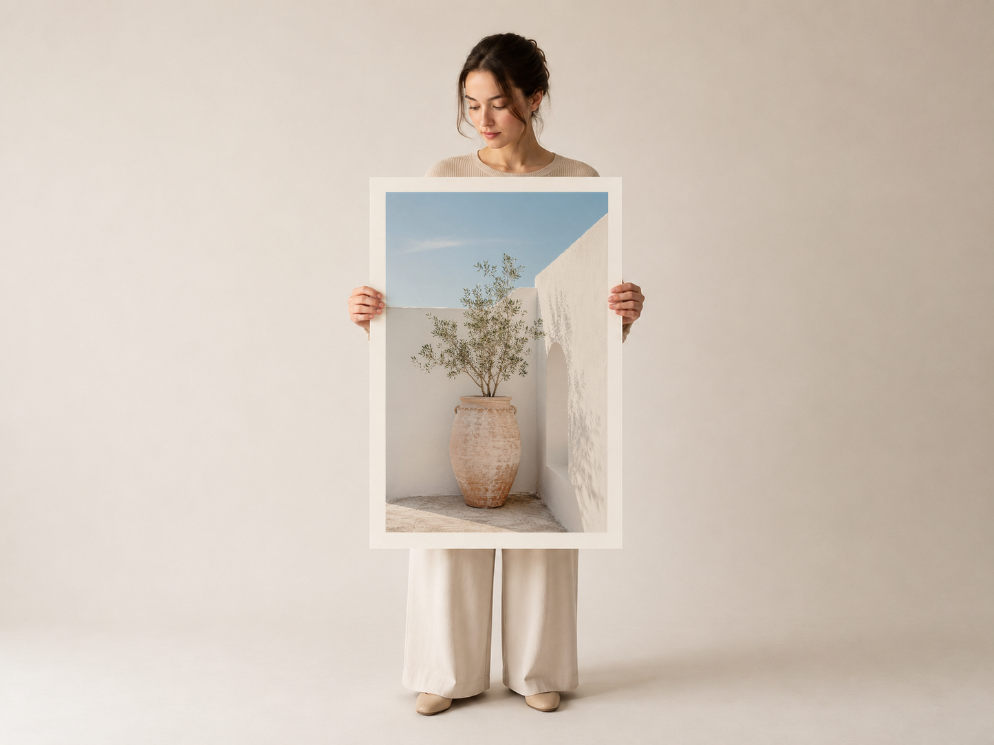 Eline aldığı beyaz çerçeveli tablonun ön görüntüsü, minimalist geometrik tasarımı ve ılık Akdeniz atmosferi.