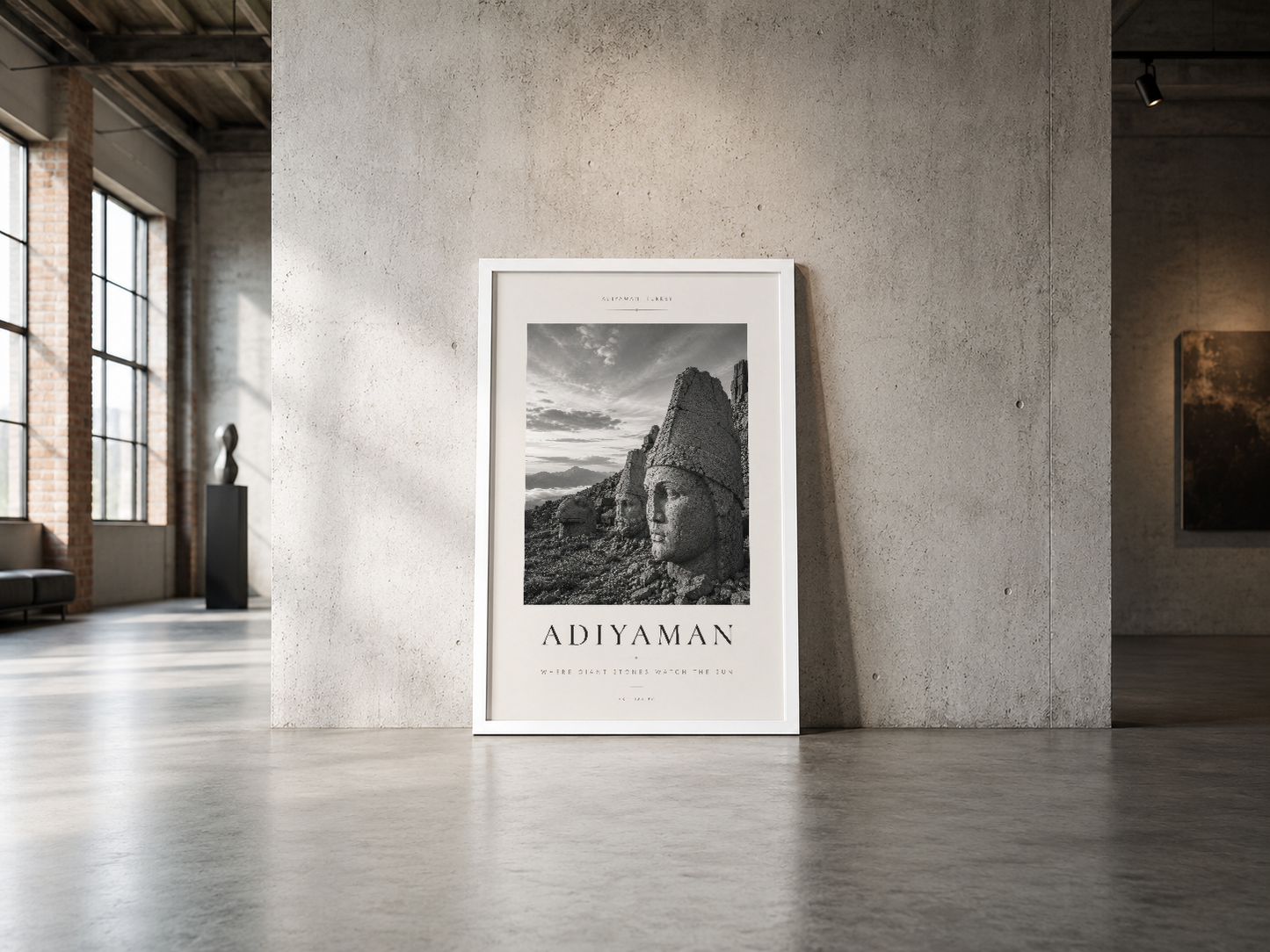 Beyaz çerçeveli Adiyaman posteri, endüstriyel beton duvarı ve geniş pencereli minimalist mekânda.
