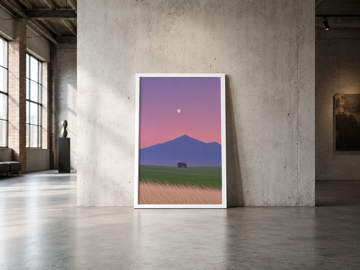 Minimalist endüstriyel alanda, beyaz çerçeveli dağ ve tarla manzarası tablosu sergileniyor.