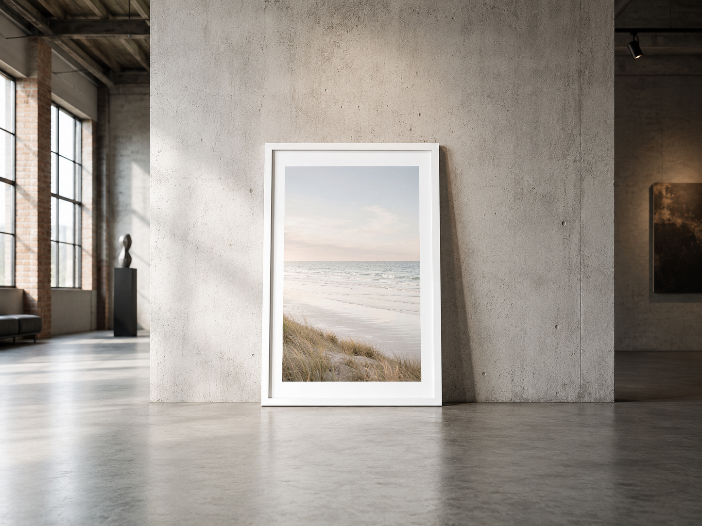 Kumlu sahil ve deniz manzaralı poster, beyaz çerçeve ile endüstriyel betonluk mekânda minimalist estetik sunmakta.