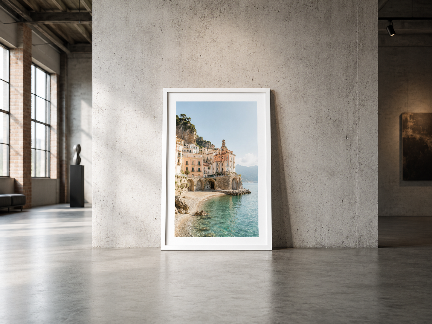 Amalfi Sahili manzarasını sunan çerçeveli poster, minimalist endüstriyel mekanda zemine yaslanmış.