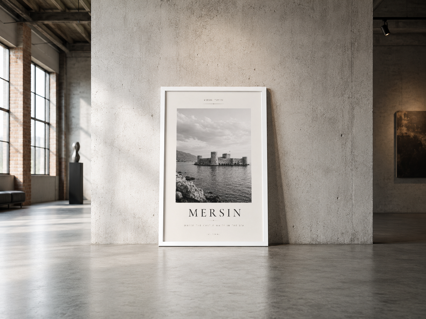 Mersin kalesi posterinin beyaz çerçevesiyle endüstriyel beton duvarın önünde minimalist bir mekan içinde sergilenmesi.