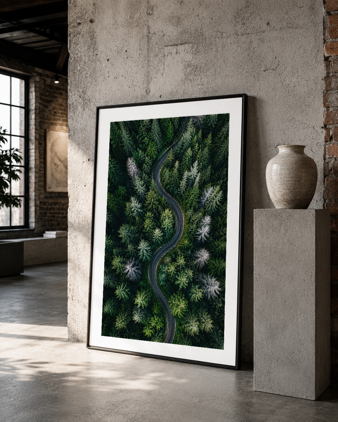 Yeşil ormanlık bölgeyi kesen asfalı yol, siyah çerçeveli duvar sanat eseri, minimalist iç mekanda.