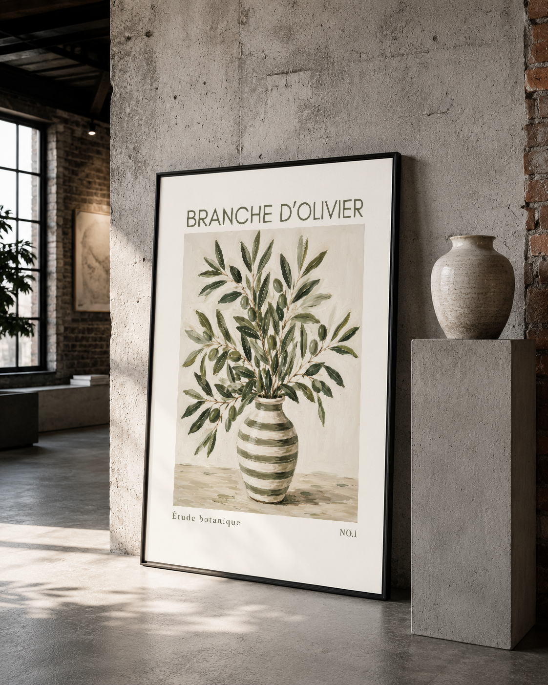 Siyah çerçeveli Branche d'Olivier tablosu, betonlu loft ortamında seramik vazonun yanına yerleştirilmiş.