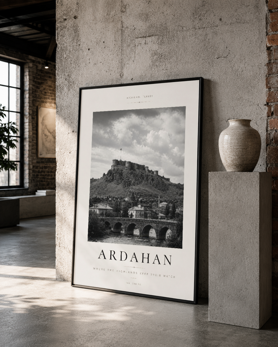 Siyah çerçeveli Ardahan tablosu, beton duvarda sanat galerisinin ihtişamı yansıtıyor.