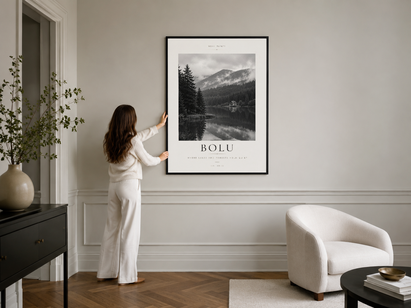 Siyah çerçeveli dağ manzarası posteri, minimalist beyaz duvarda asılı olup modern oturma alanını süslüyor.