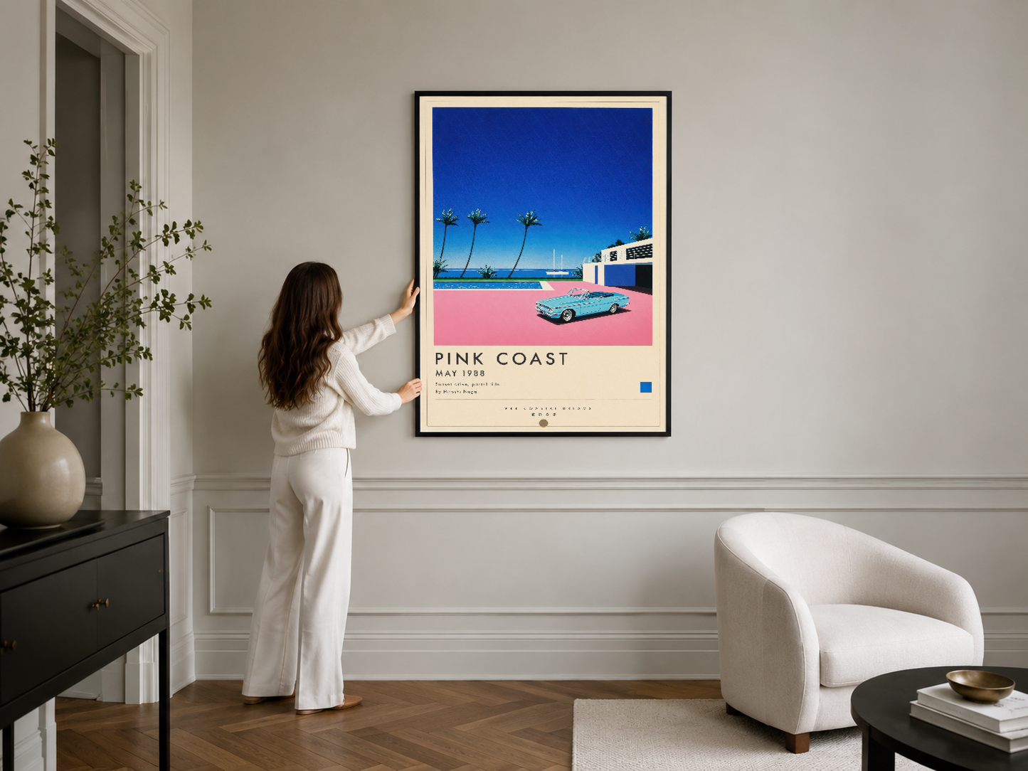 Siyah çerçeveli retro Pink Coast tablosu, modern oturma odasında beyaz koltuk ve cihazlarla zarif iç mimar dekorasyonu.