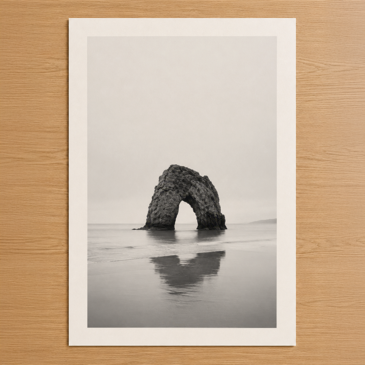 Siyah beyaz deniz fotoğrafası: kayalık kaya arkı sessiz kıyıda, minimalist ve sakin atmosfer.
