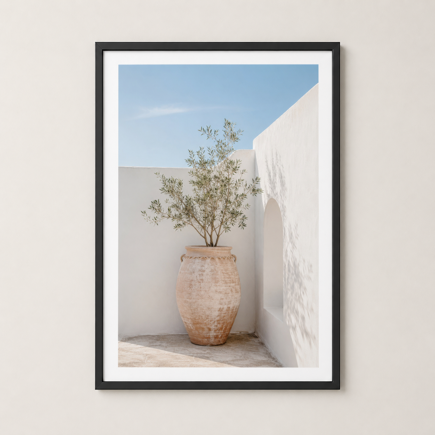 Siyah çerçeveli poster, beyaz duvar önündeki terrakotta saksıda zeytin bitkisi ve geometrik mimari detayları.