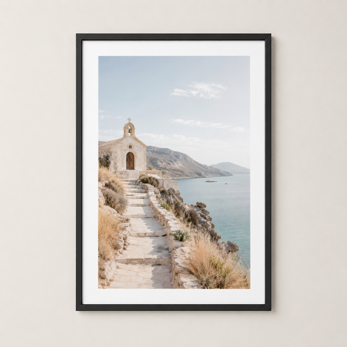 Coastal white chapel on stone stairs overlooking turquoise sea, framed in black