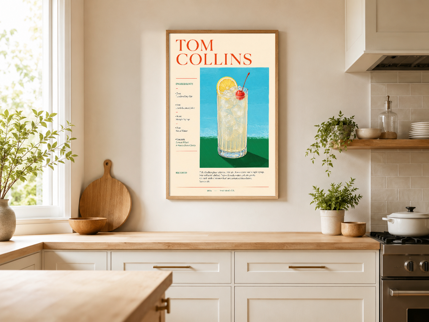 Tom Collins posteri modern mutfakta ahşap çerçevede, raflı beyaz dolapların üstünde.