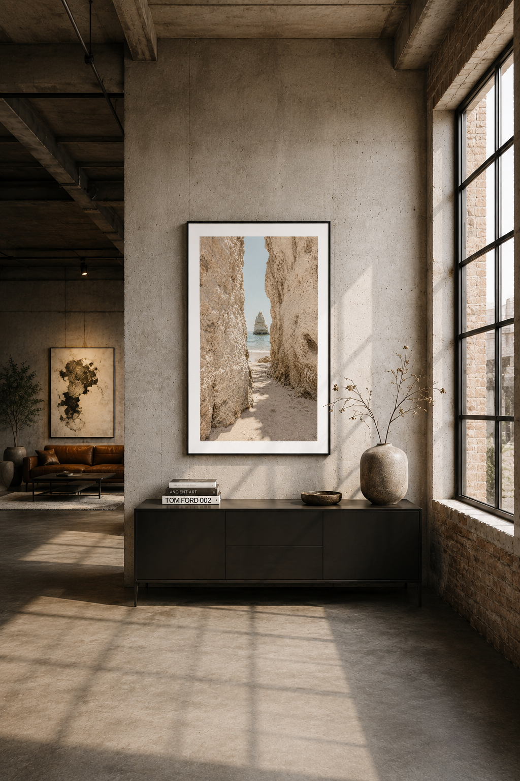 İndüstriyel loft alanında, siyah dolap üstünde asılan tabloda sahil kayalıkları ve deniz manzarası görülüyor, minimalist iç