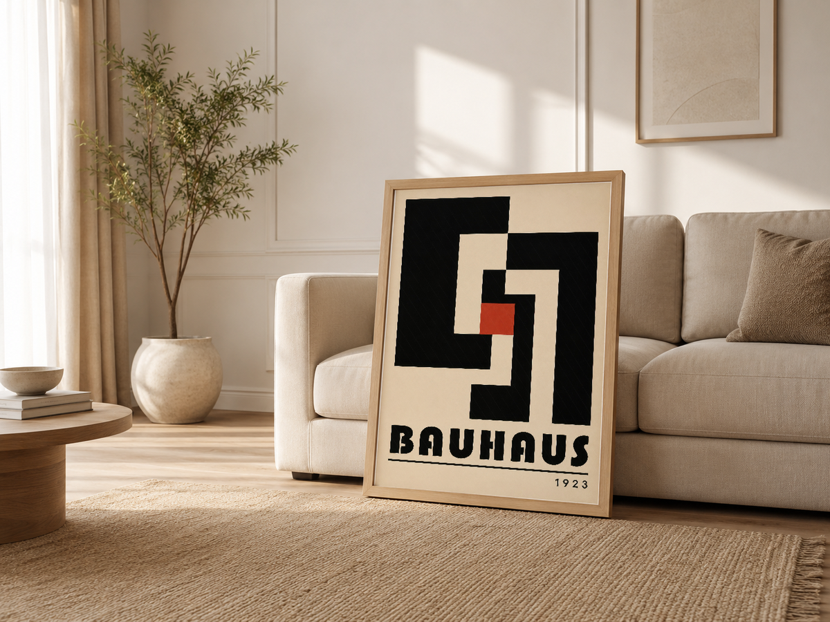 Açık renkli oturma odasında, kanepenin yanına yaslanmış ahşap çerçeveli Bauhaus tablosu.