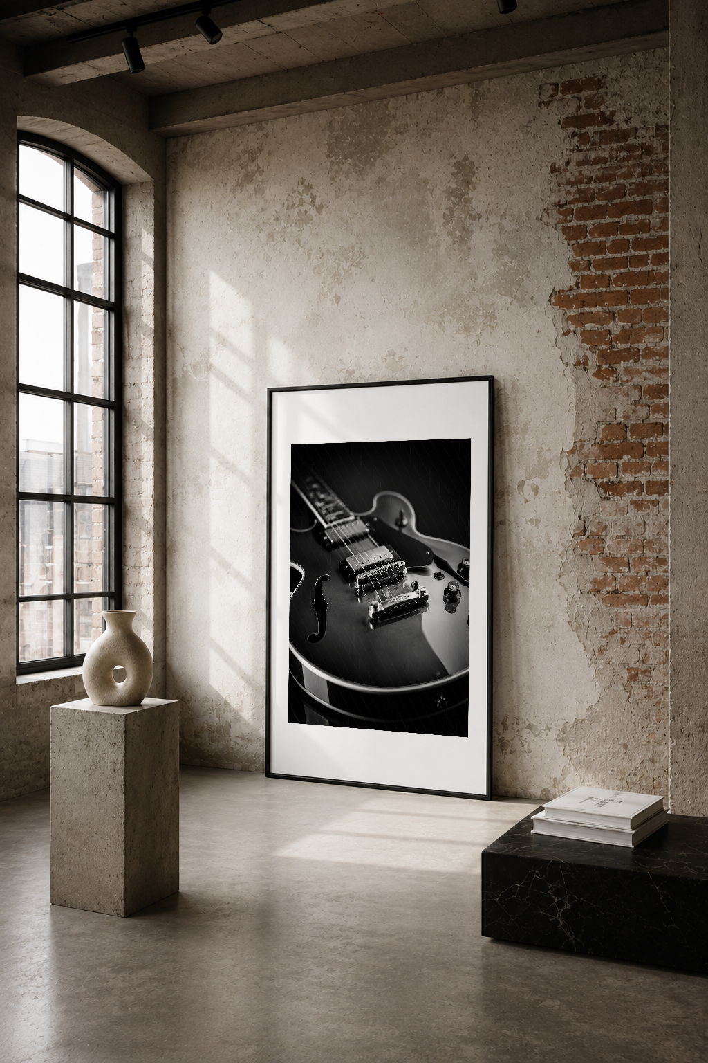 Siyah beyaz elektrik gitar detayı, endüstriyel mekanın beyaz duvarına siyah çerçevede asılı.